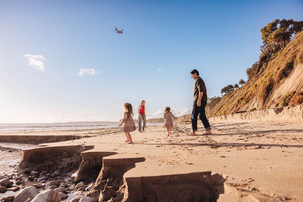 People walking along a scenic coastal beach trail with eroding cliffs and ocean views on a sunny day.