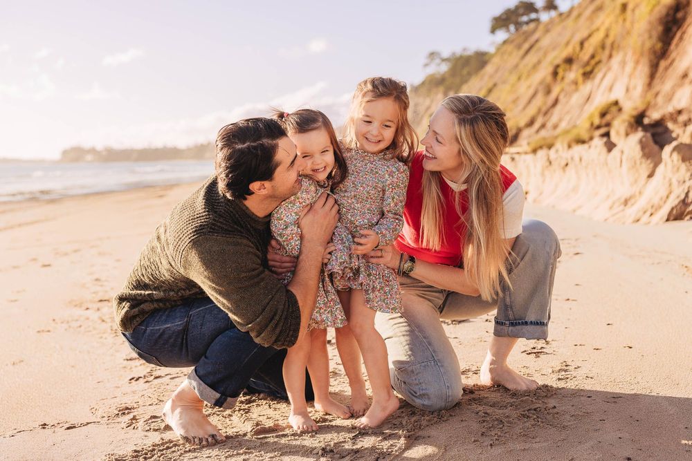 Family sharing tender moment together on sandy beach near coastal cliffs.