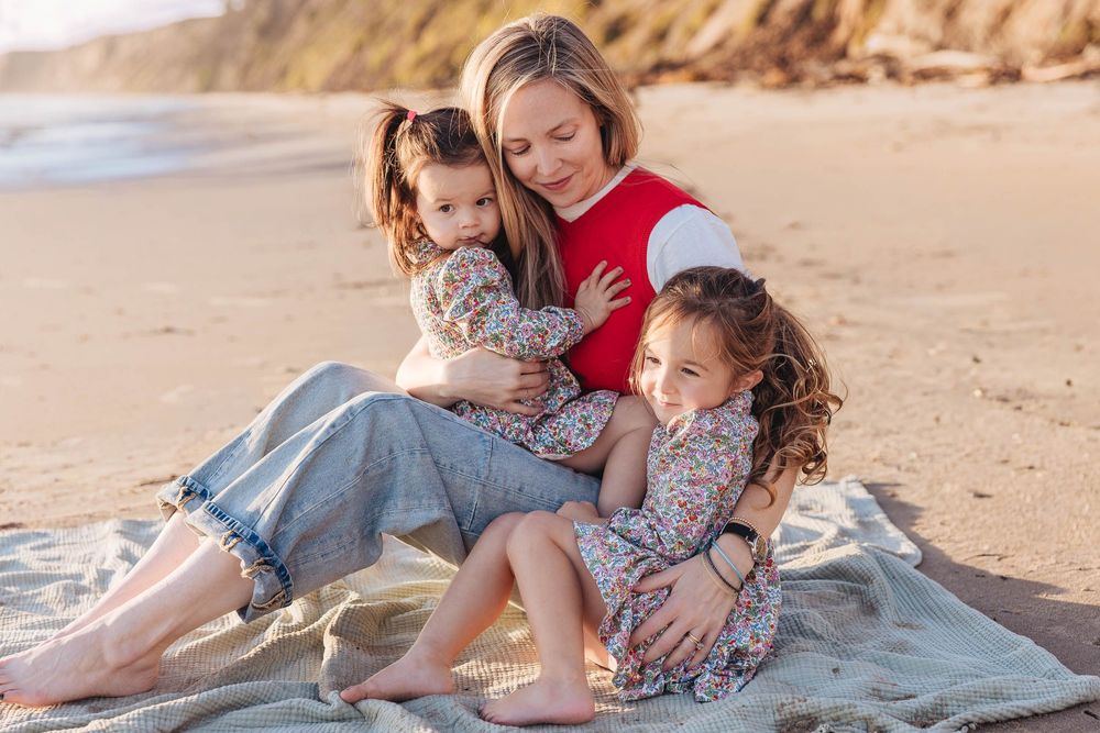 Tender family moment sitting together on blanket at scenic beach during golden hour.