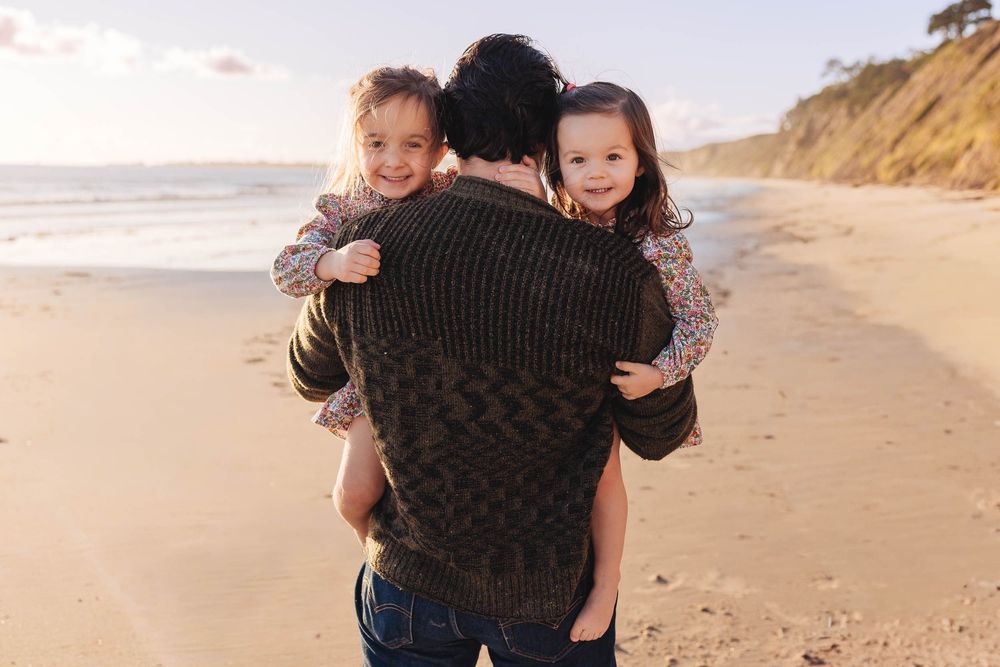 Joyful piggyback ride moment on sandy beach with cliffs in background.