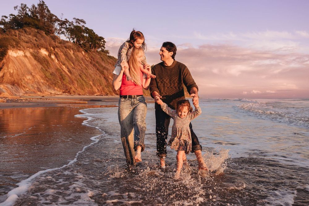 Family splashing through waves together on beach at golden hour.