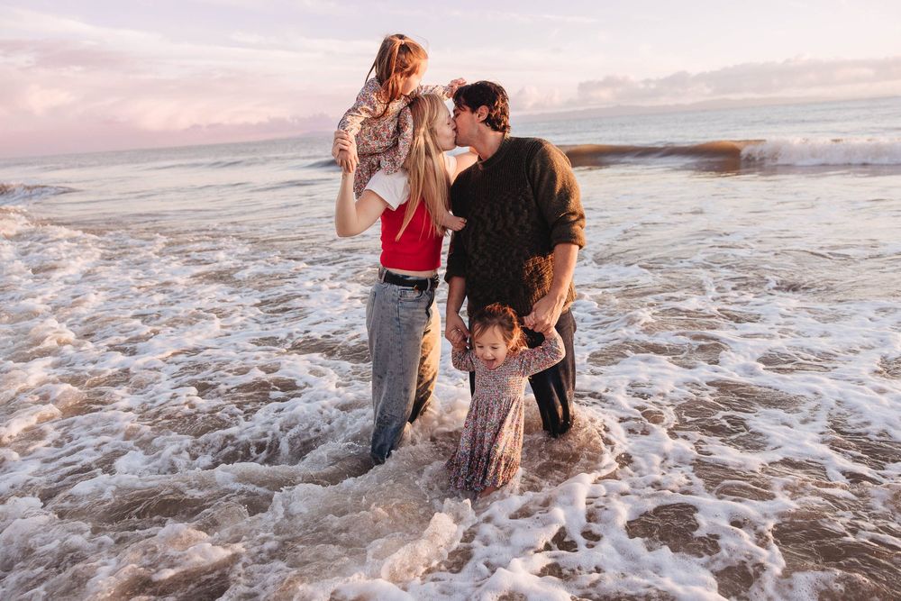 Family playing together in ocean waves during sunset at the beach.