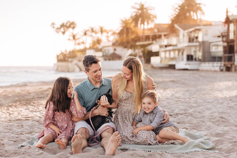 A family relaxes together on a sandy beach during sunset, creating a warm and intimate moment.