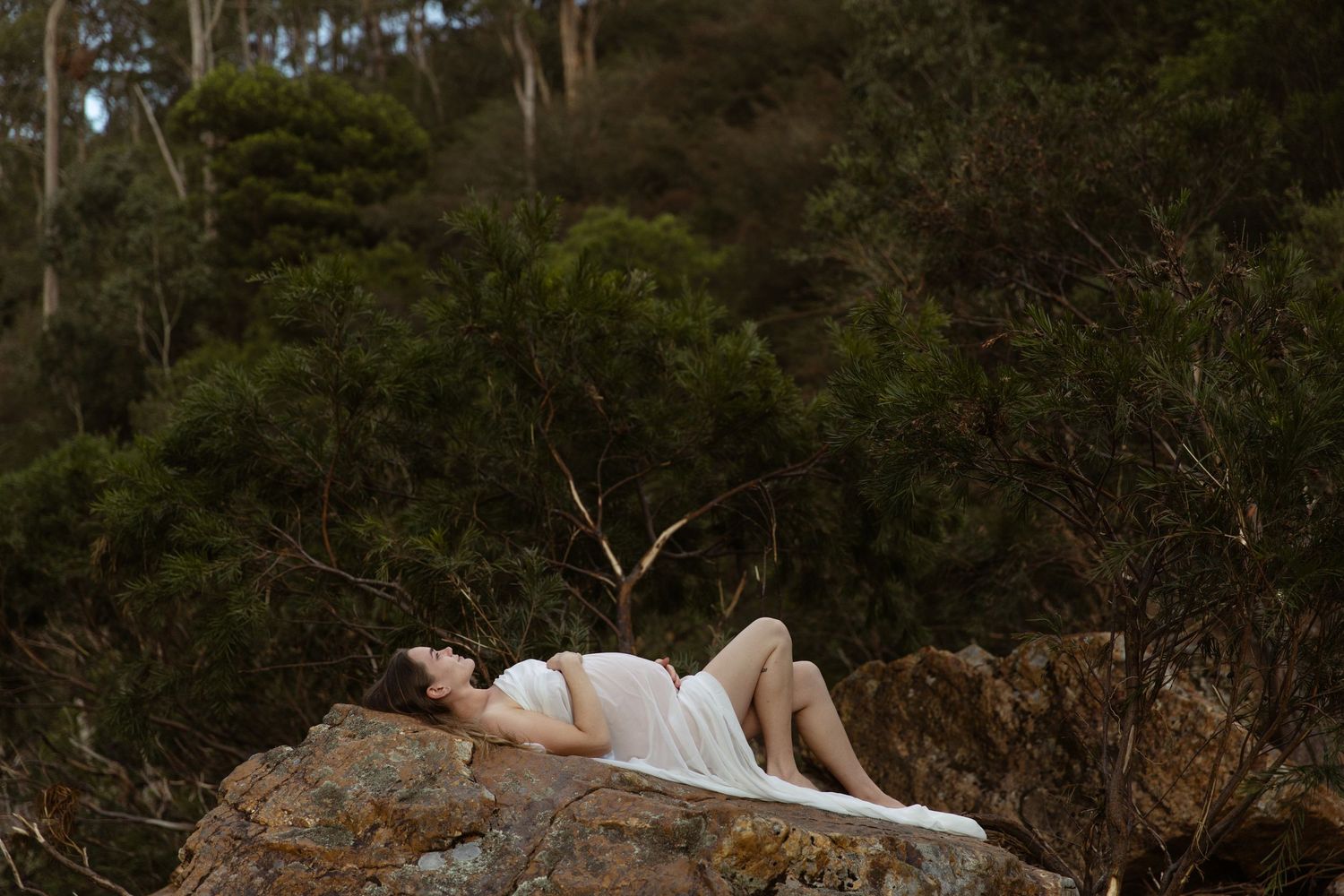 A pregnant mother lays back on a boulder, during a maternity photography session in Gippsland, Vic