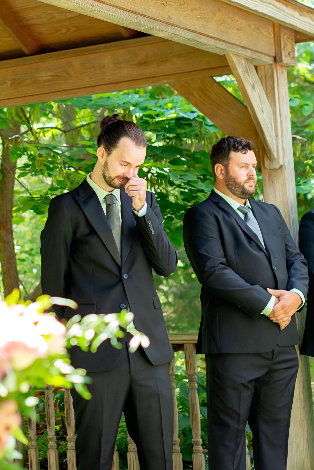 Groomsmen in black suits stand casually on an outdoor wooden deck at Elsie Perrin Williams Estate in London.