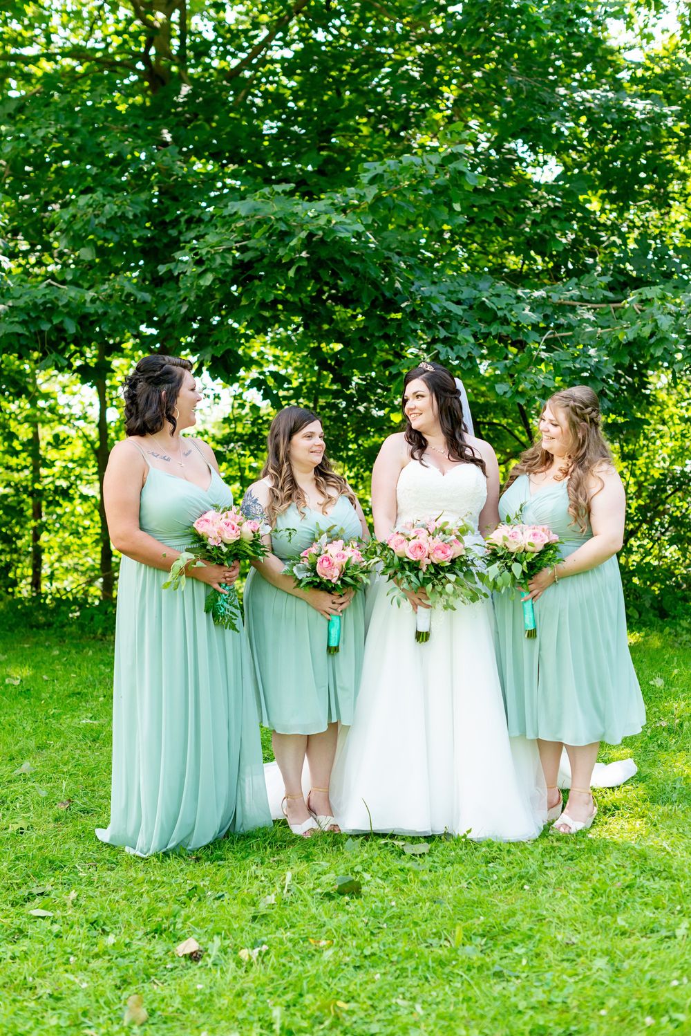 Bridesmaids in mint green dresses hold pink bouquets while standing on grass at Elsie Perrin Williams Estate in London.