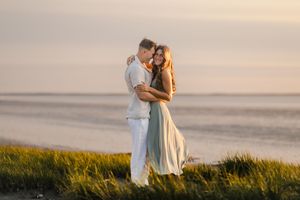Romantic couple embraces on coastal marshy view in Saint Helena, South Carolina during golden sunset while tall grass sways in the breeze.