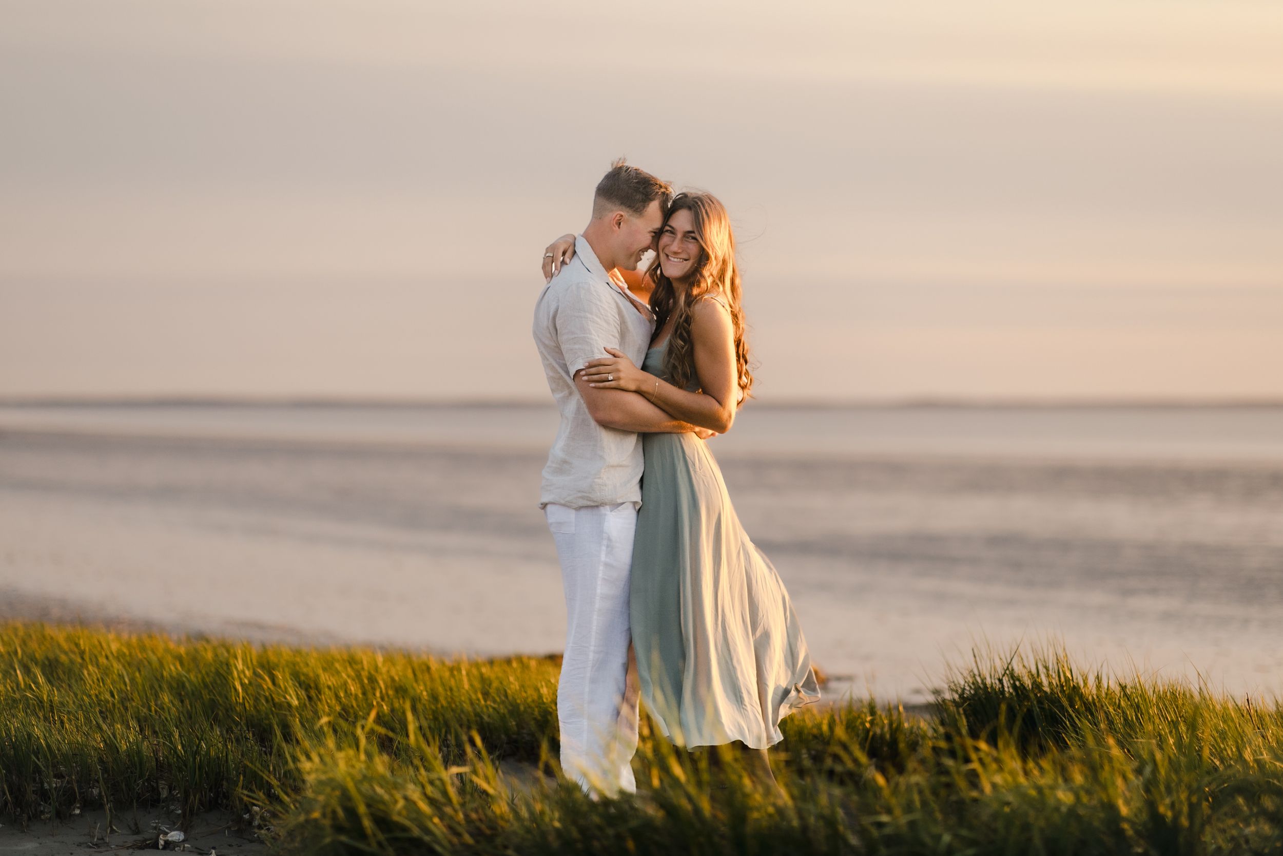 Romantic couple embraces on coastal marshy view in Saint Helena, South Carolina during golden sunset while tall grass sways in the breeze.