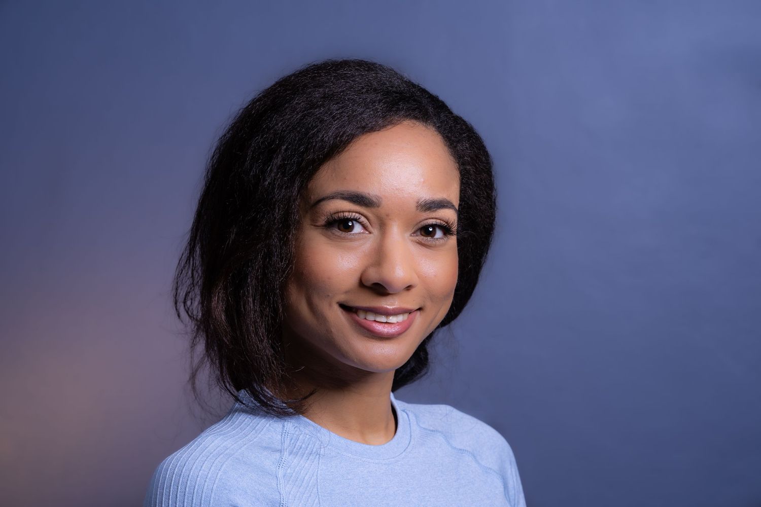 Portrait photography of a woman with dark hair and a blue top smiling to camera