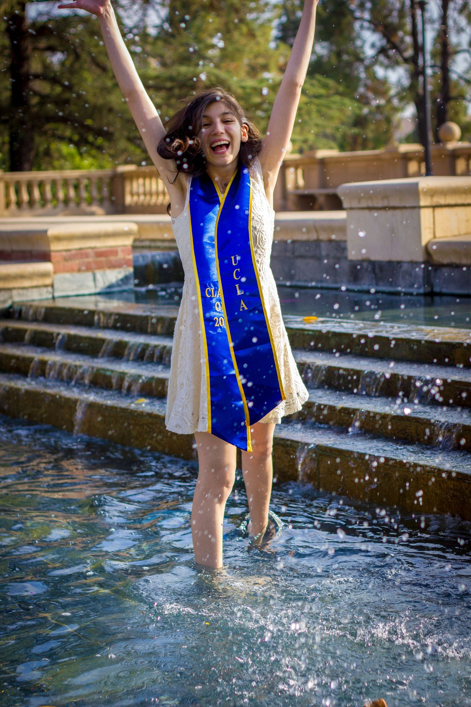A graduate wearing a blue sash splashes in the fountain at UCLA.