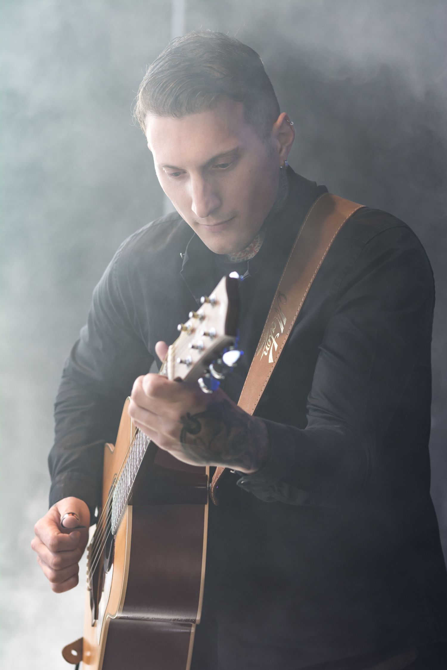 A musician performing in smoky atmospheric lighting plays acoustic guitar while wearing a black shirt.