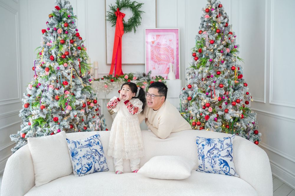 Elegant Christmas photo setup with two decorated trees flanking a white couch with blue and white decorative pillows.