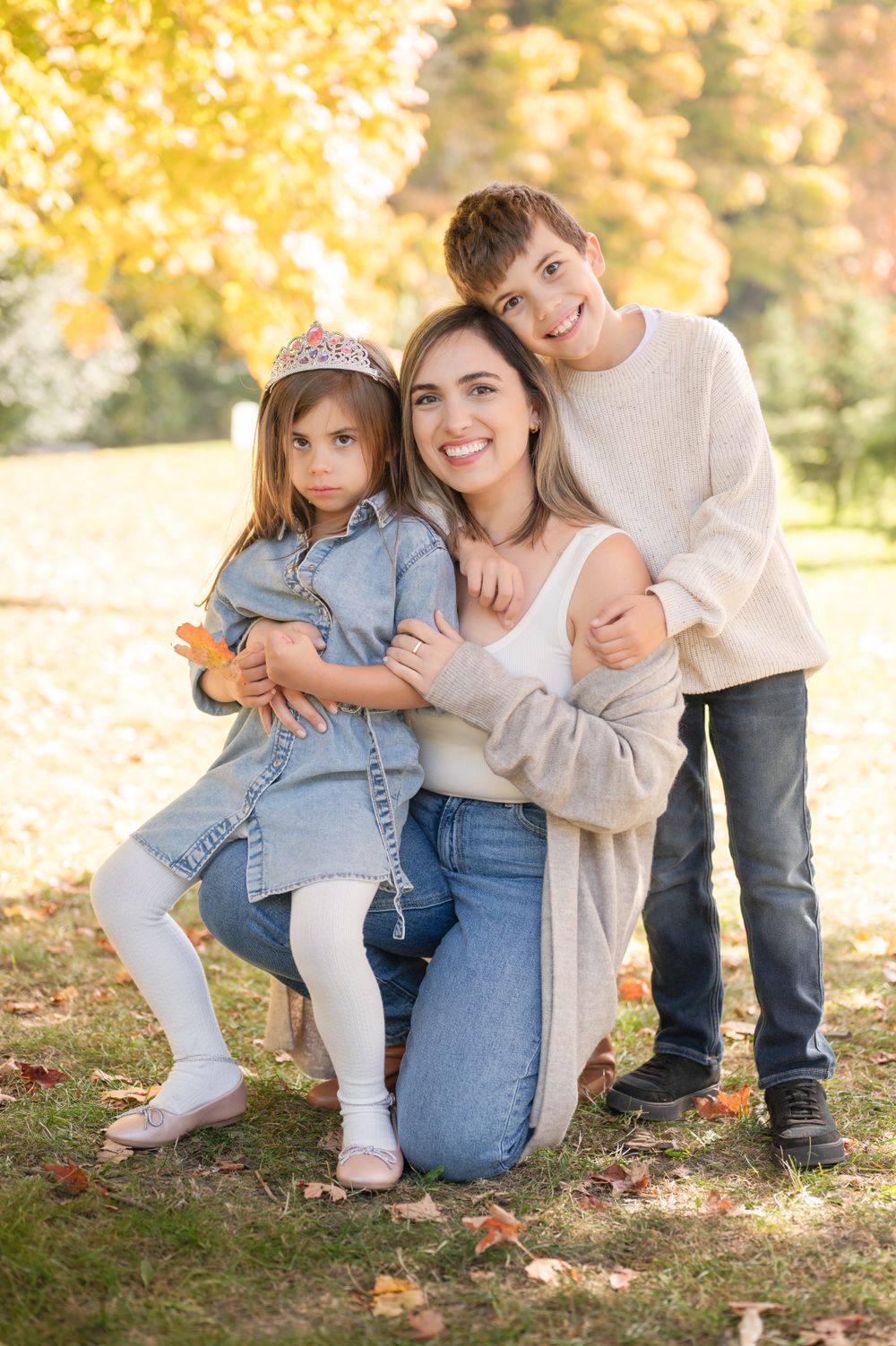 A family poses together outdoors on an autumn day with golden yellow foliage in the background.