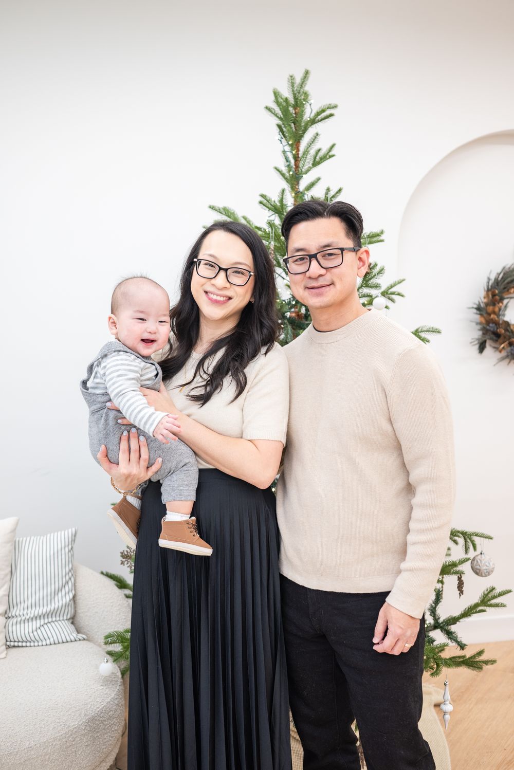 Family portrait taken indoors with a baby, featuring modern decor including a green plant and light gray background.
