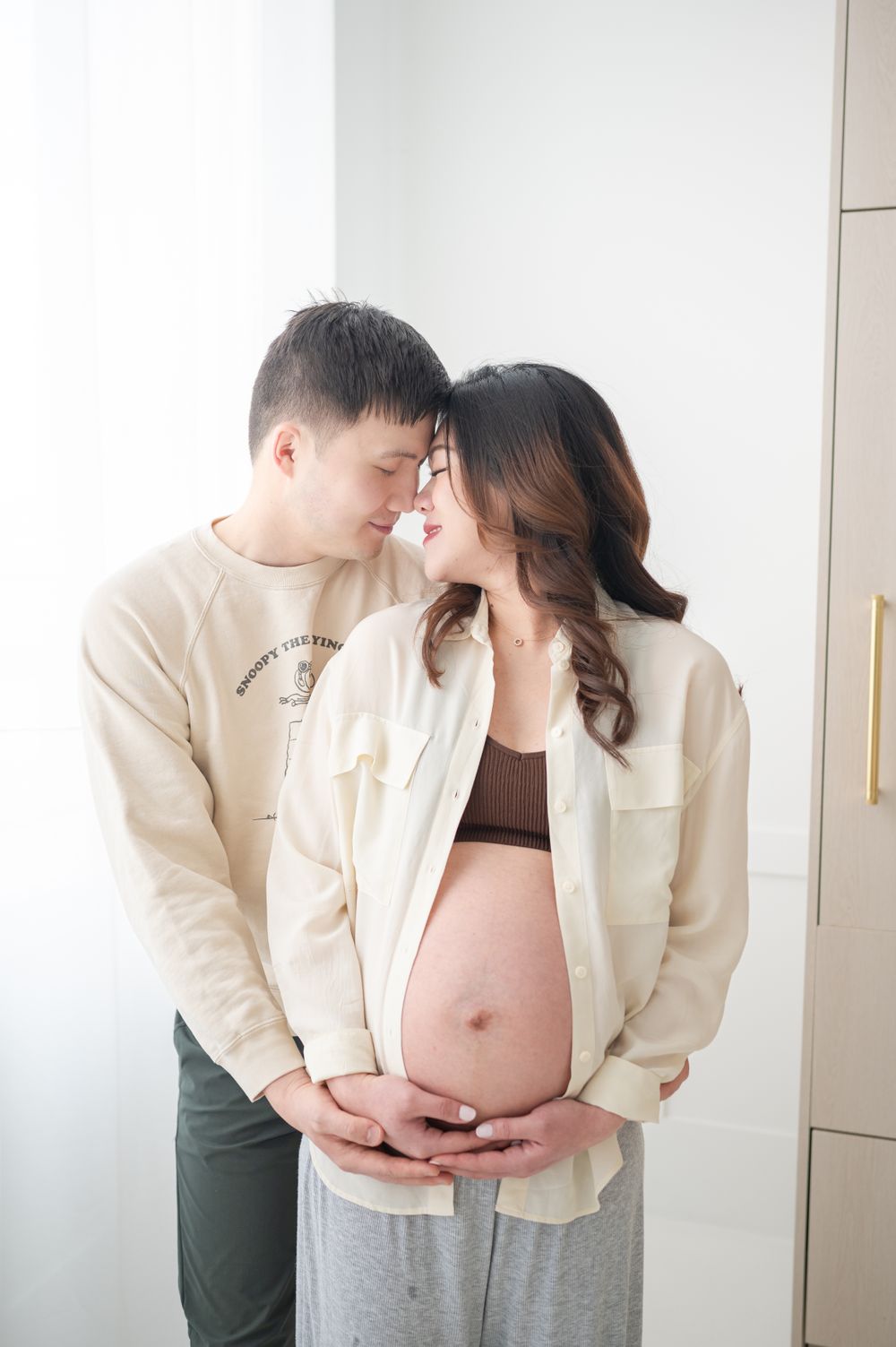 A tender maternity moment captured as a couple shares an intimate embrace by a bright window.