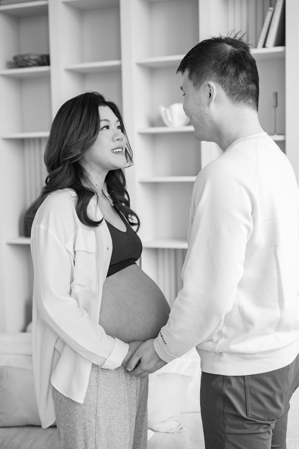A tender black and white pregnancy photo showing an intimate moment between a couple near white bookshelves.