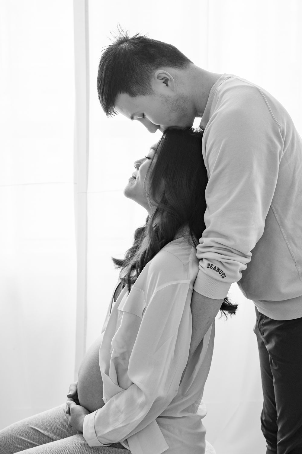 Black and white artistic portrait of a romantic intimate moment between a couple in white clothing.