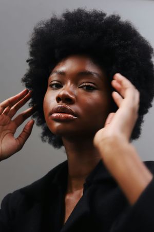 Close-up portrait of person with natural afro hairstyle touching their face against grey background.