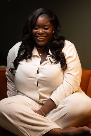 Portrait of person in white outfit sitting comfortably on leather chair with joyful expression.