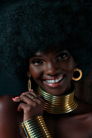 Artistic portrait with natural afro hair and gold neck jewelry against dark background.