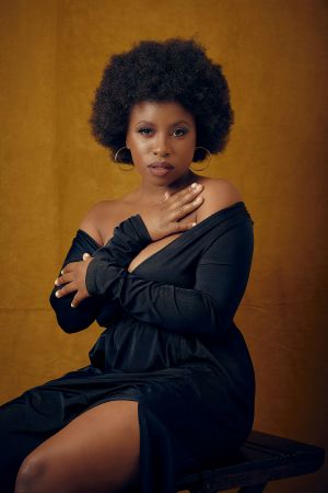 Artistic portrait against gold background featuring elegant black evening dress and natural afro hairstyle.