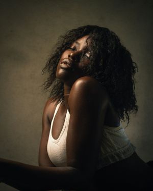 Artistic portrait with natural curly hair in white tank top against textured background.