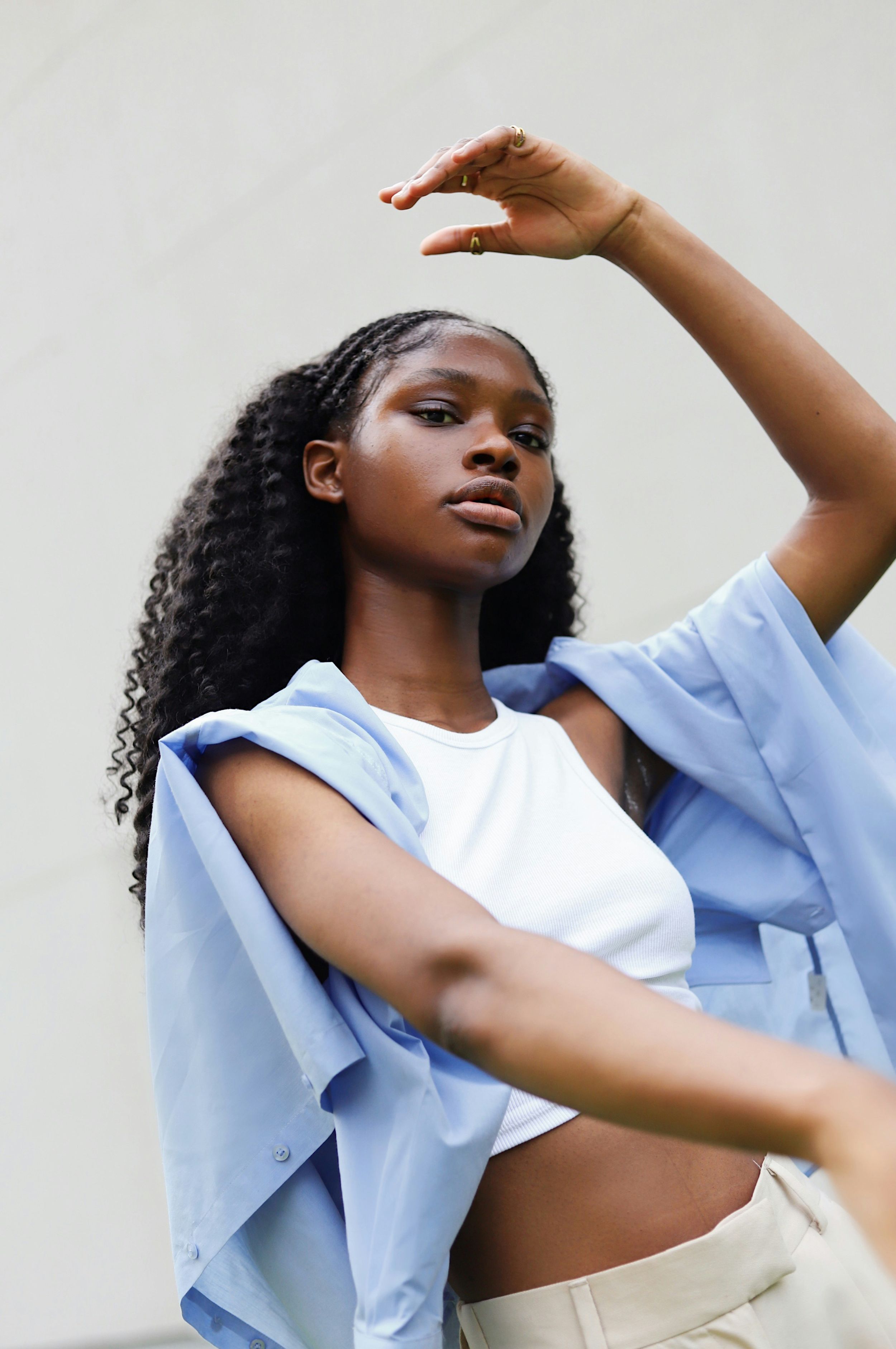 Fashion portrait in casual white and light blue outfit with raised arm gesture.