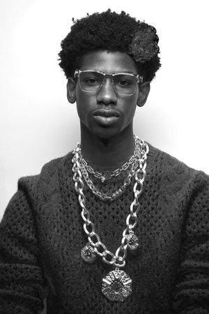 Black and white portrait featuring glasses and layered silver chain necklaces.