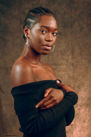 Portrait in off-shoulder black sweater with braided hair and delicate jewelry.