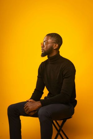 Professional studio portrait of person in black turtleneck against vibrant orange background.