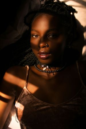 Moody portrait featuring delicate necklace and nose ring in warm lighting.