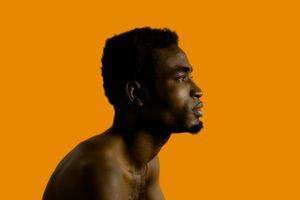 Dramatic profile silhouette against bright orange background in studio lighting.