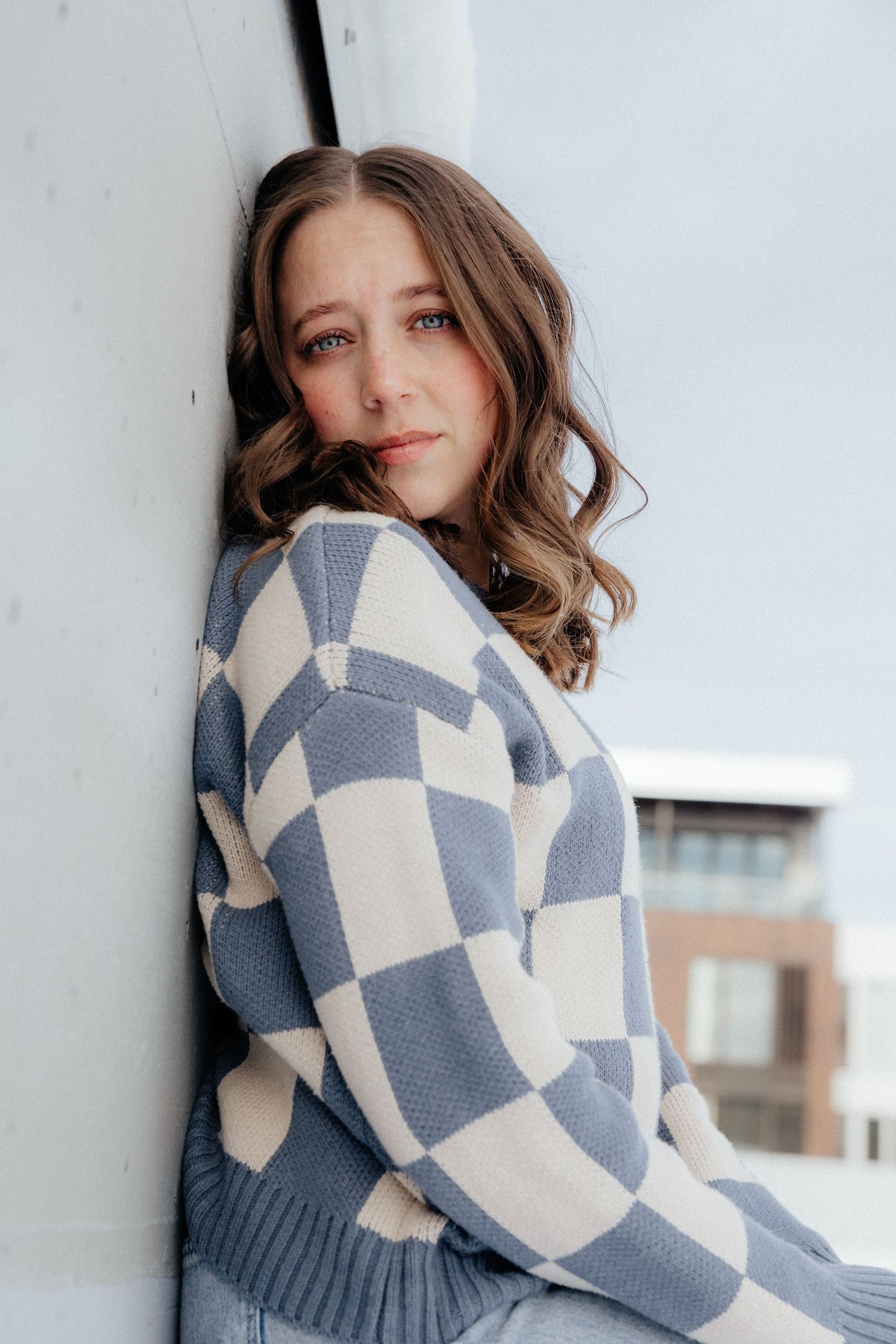 A person in a cozy blue and cream checkered sweater poses against a white wall on a winter day.