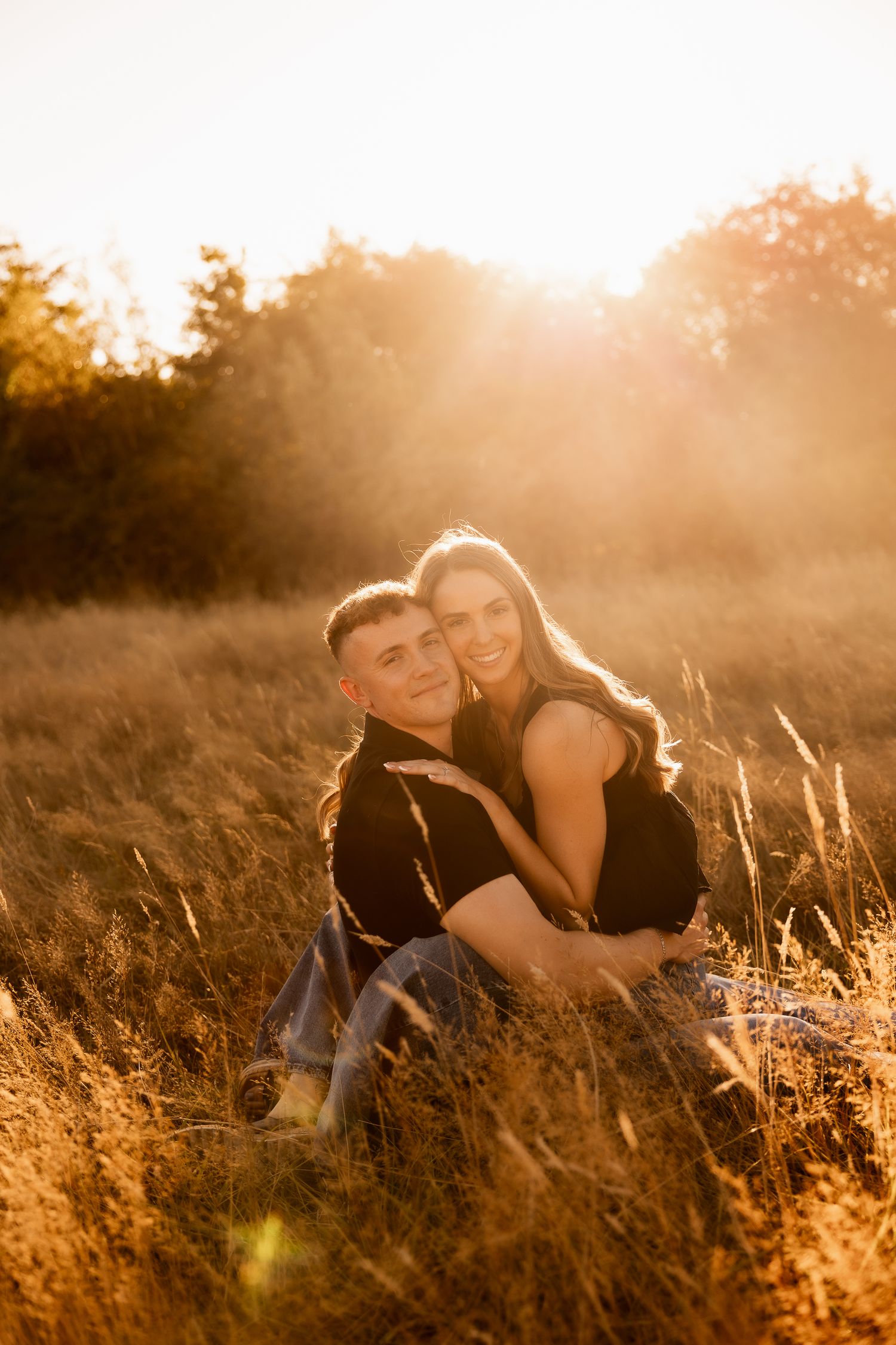 A couple embraces in a golden sunlit field during sunset creating a romantic silhouette against the warm glowing sky.