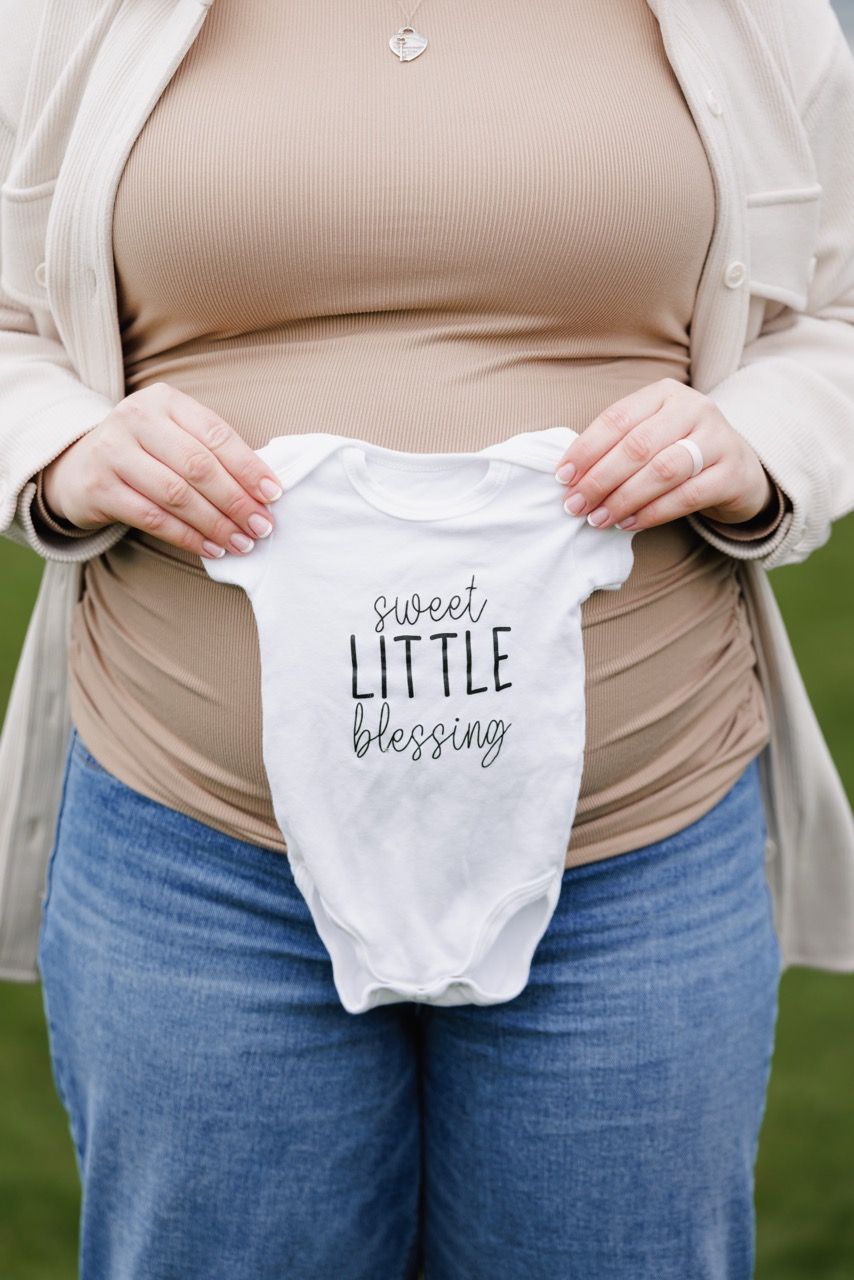 Expecting mother holding baby outfit in front of pregnant belly during maternity session in Mukilteo WA