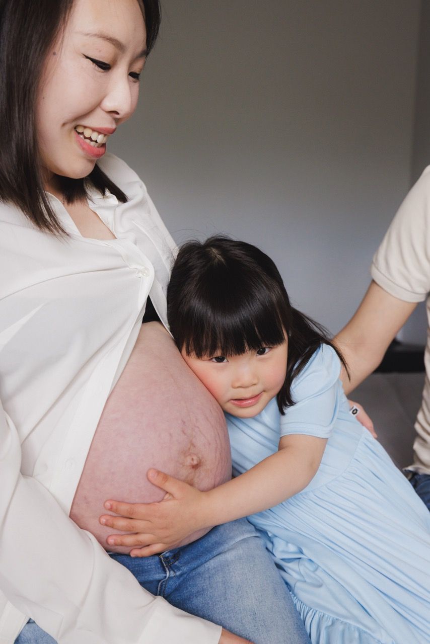 Toddler hugging mother's baby bump in a Snohomish home. Affectionate family maternity session by Tim Neal.
