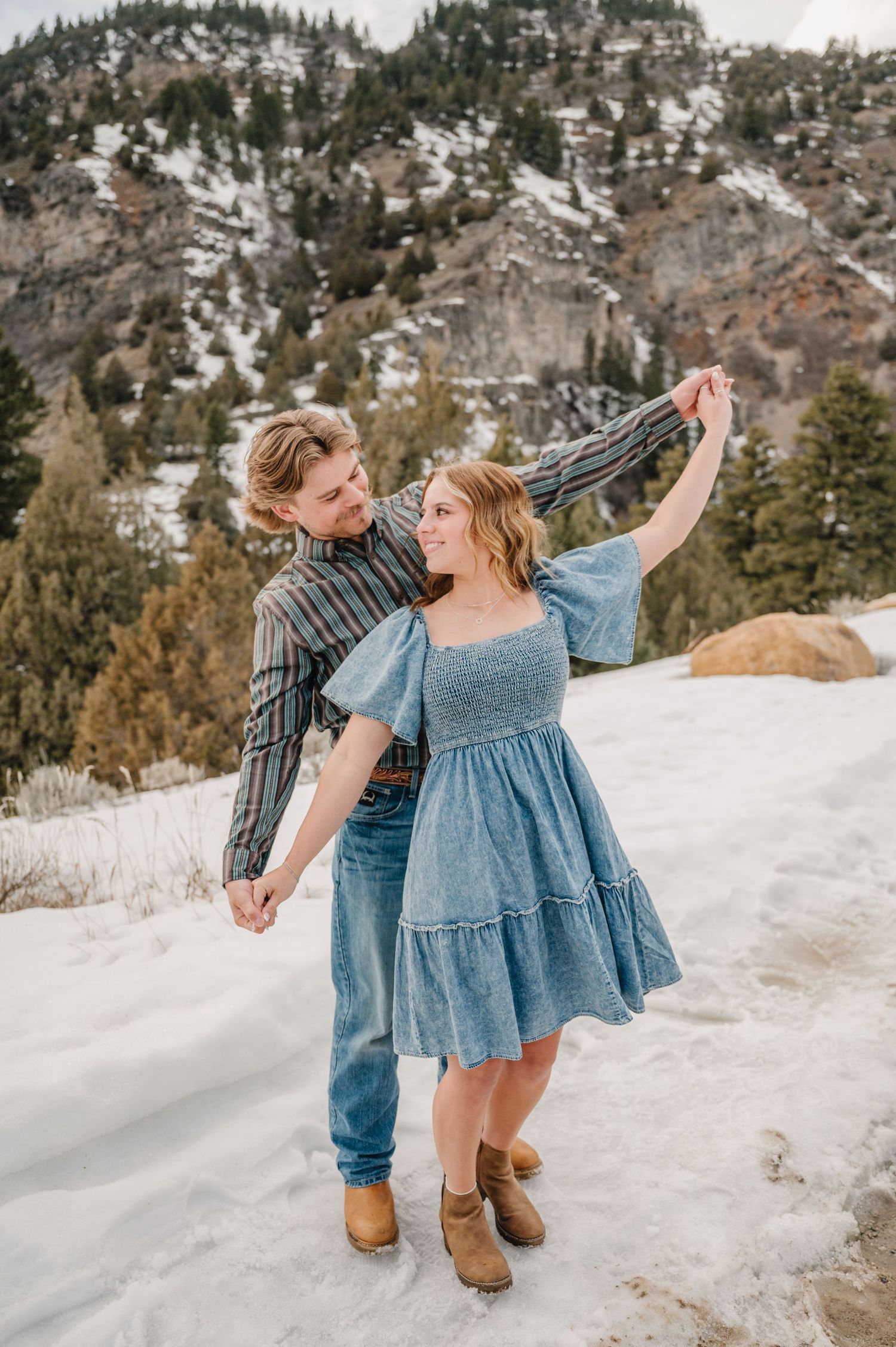 Dancing together in the snowy mountains, a couple twirls in front of a scenic winter forest backdrop.
