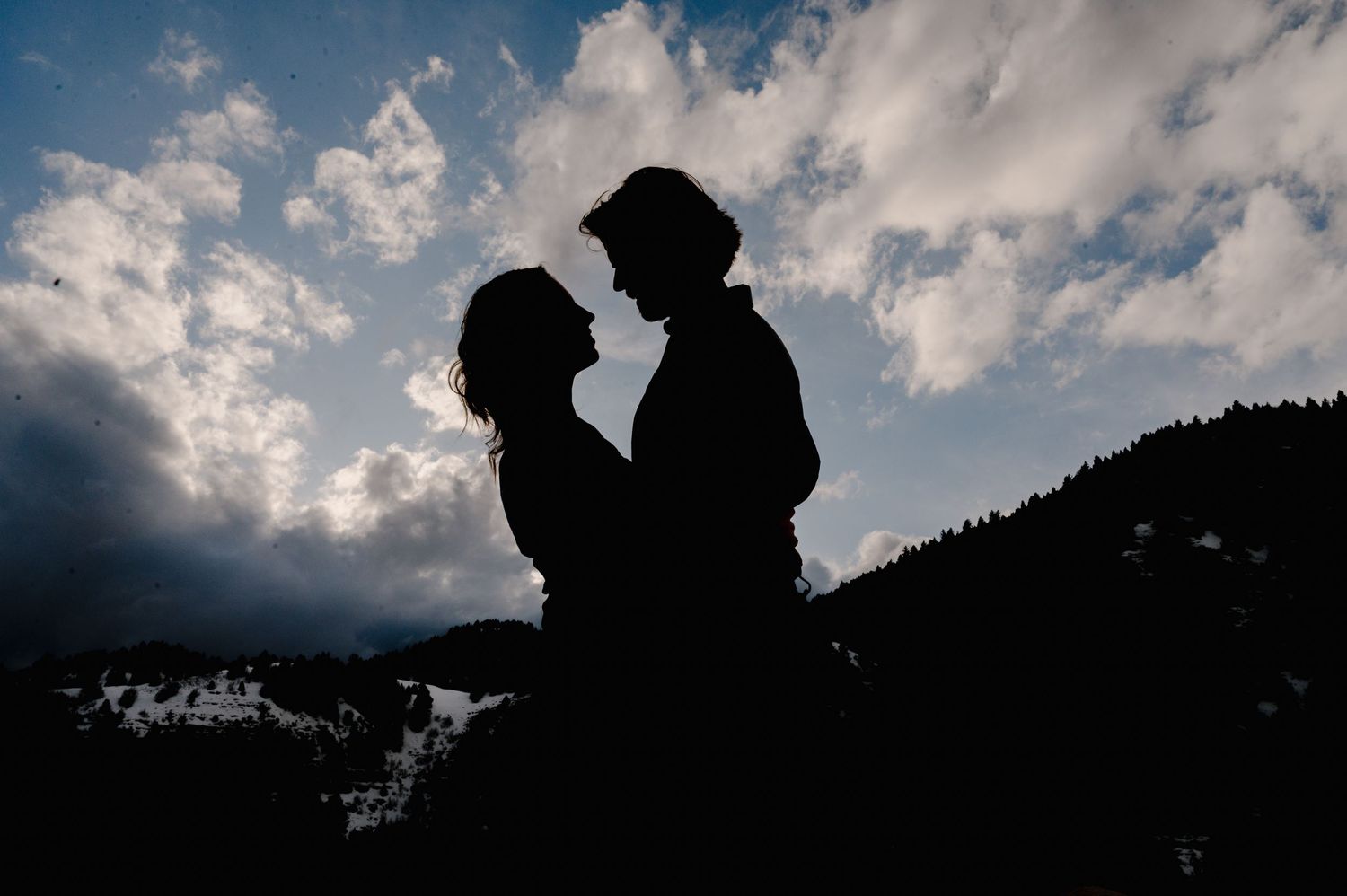 A romantic silhouette of a couple against a dramatic cloudy sky with mountains in the background.