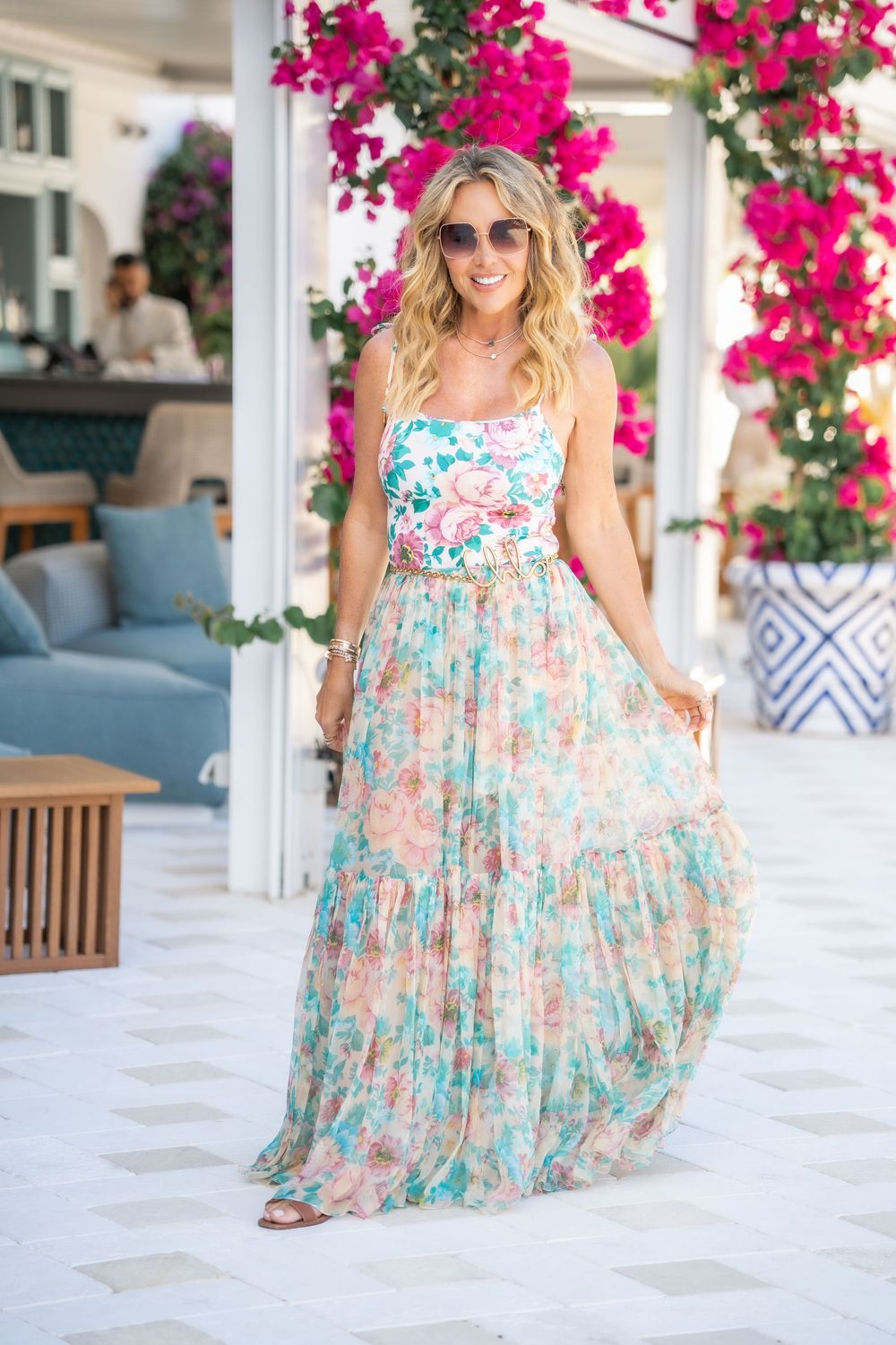 A floral maxi dress is showcased on a patio with bright pink bougainvillea flowers and coastal decor.