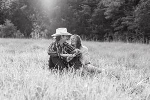 Couple sits together in sunlit grassy field in romantic black and white outdoor portrait.