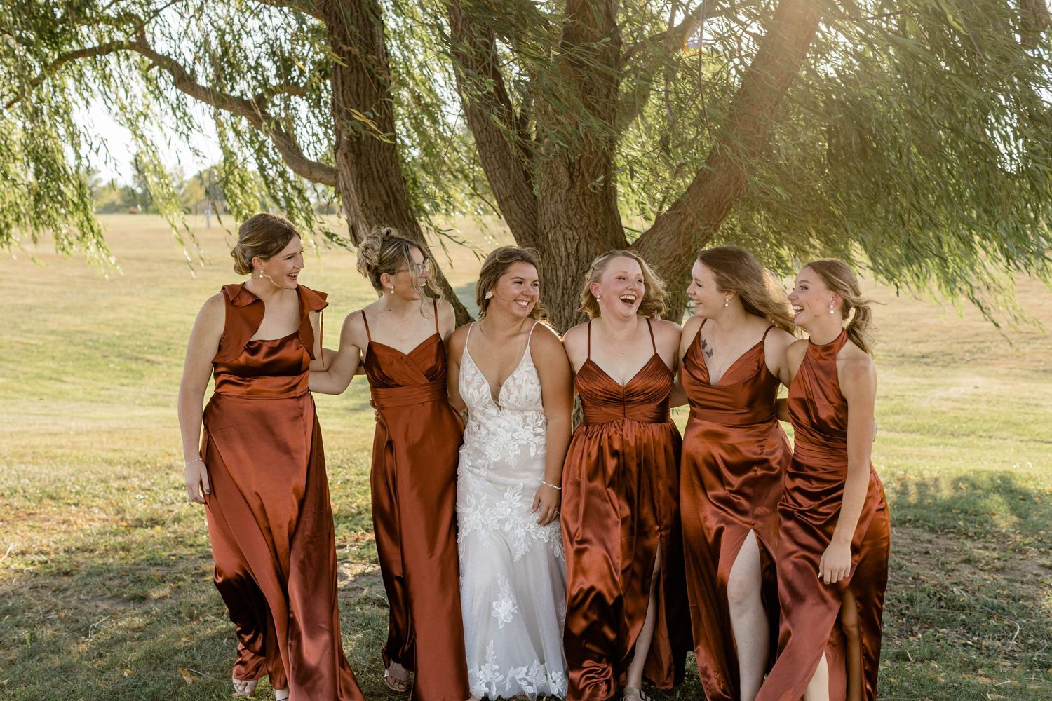 Bridesmaids wearing soft pastel dresses stand together holding floral bouquets.