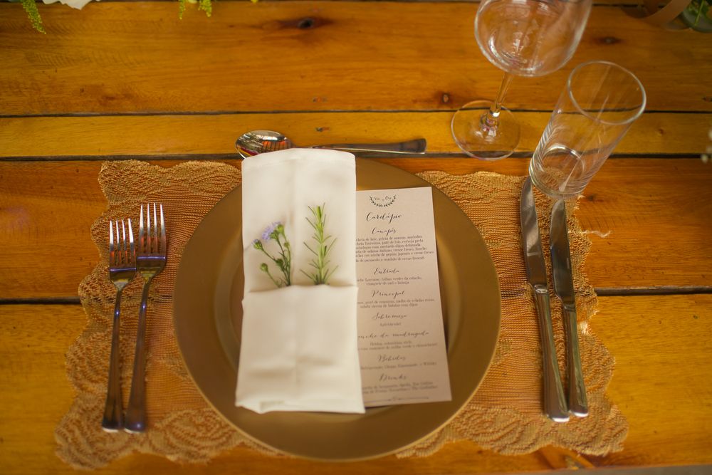 Place setting with menu card and greenery on wooden table at rustic wedding reception.