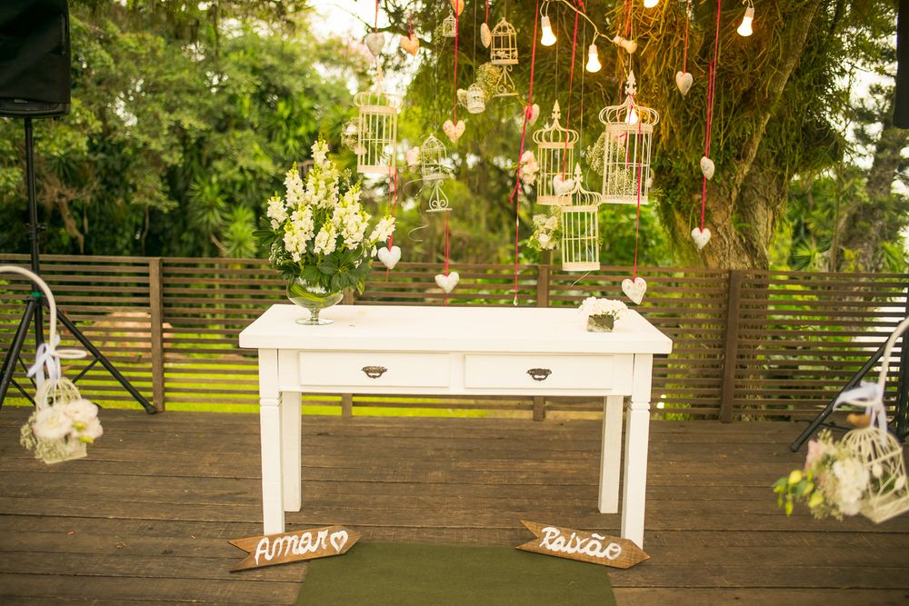 White vintage desk decorated with hanging lights and floral arrangements for outdoor wedding.