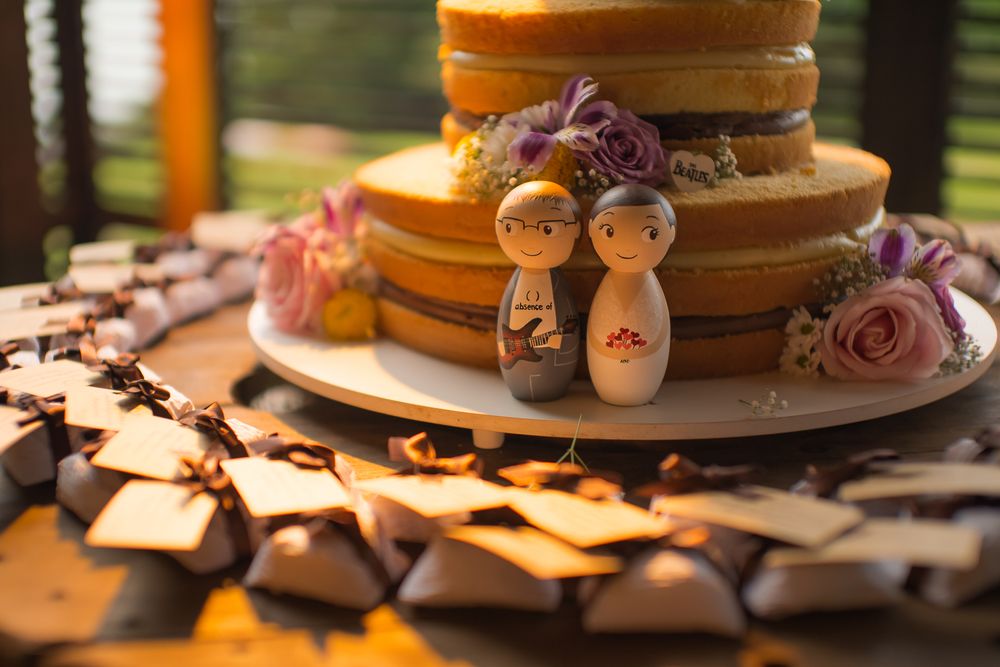 Wedding cake topped with wooden figurines and decorated with purple roses.