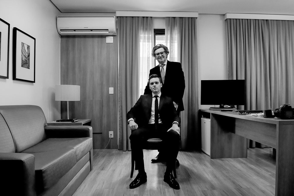Two people in formal attire pose in a modern hotel room interior with minimalist decor.