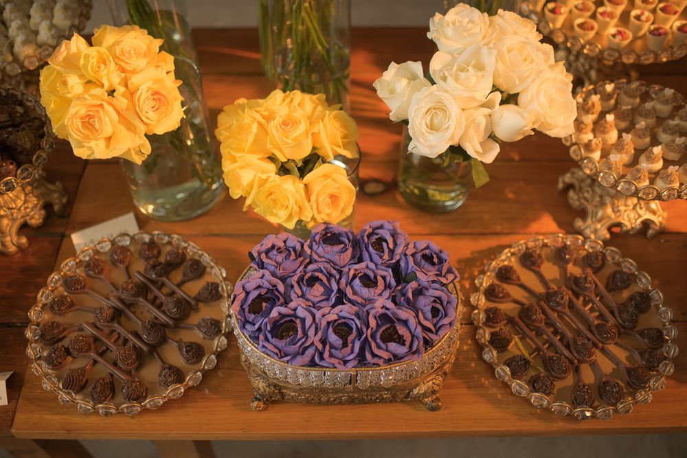 Wedding dessert table with purple roses and sweets arranged on decorative silver platters.