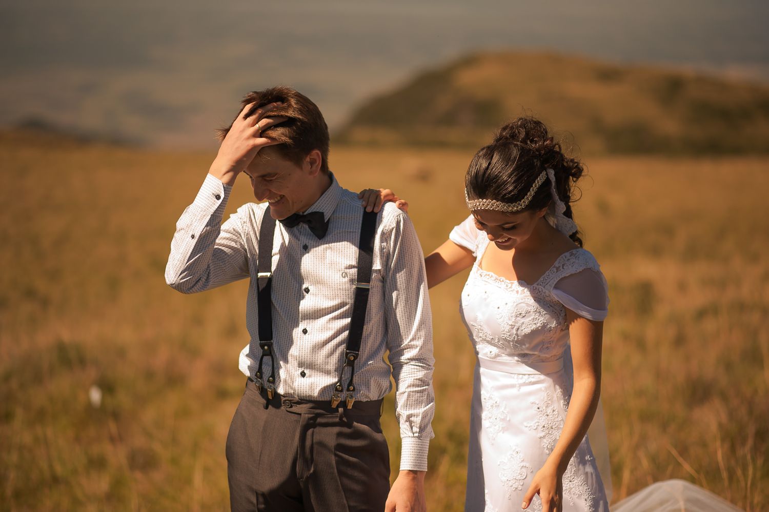 A candid moment shared between a couple in formal attire on a grassy hillside.