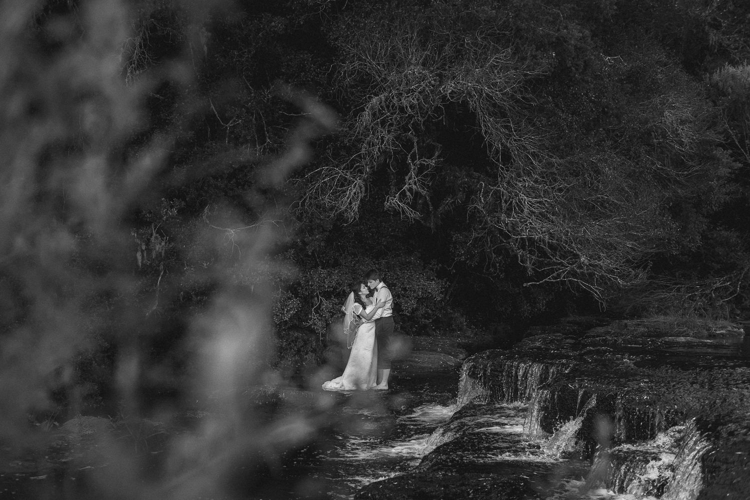 A romantic moment captured in black and white near a scenic waterfall.