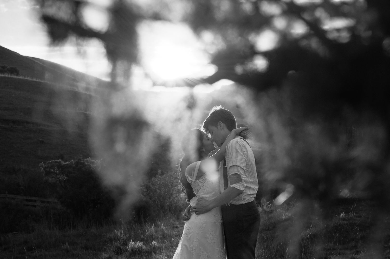 Romantic black and white portrait with sunlight filtering through trees creating dramatic shadows.