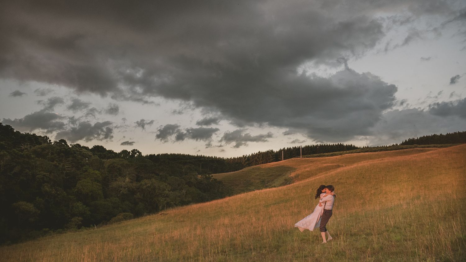 A dramatic wedding scene on a hillside with stormy clouds overhead.